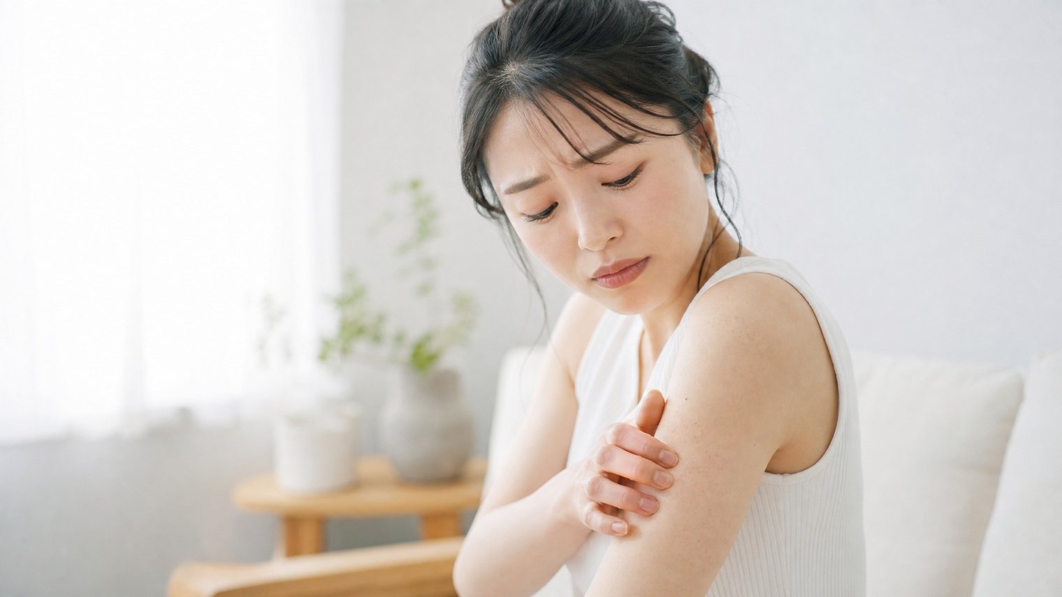 明るい室内で二の腕に手を添える女性。二の腕のぶつぶつが気になる場面のイメージ写真。
